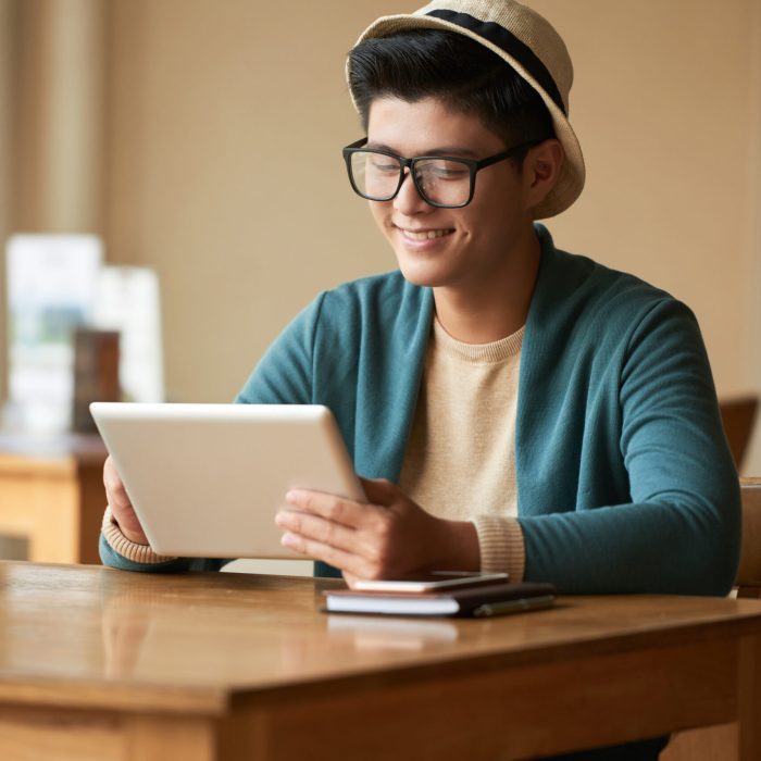 Handsome smiling young Asian man watching video on tablet computer